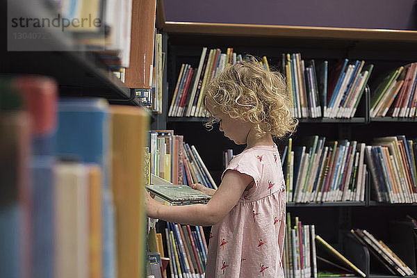 Seitenansicht eines Mädchens  das ein Buch betrachtet  während es in der Bibliothek steht