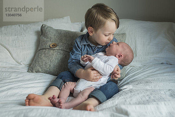 Junge sitzt mit neugeborenem Bruder zu Hause im Bett