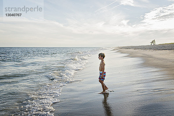 Seitenansicht eines Jungen ohne Hemd  der weg schaut  während er am Tobay Beach gegen den Himmel steht