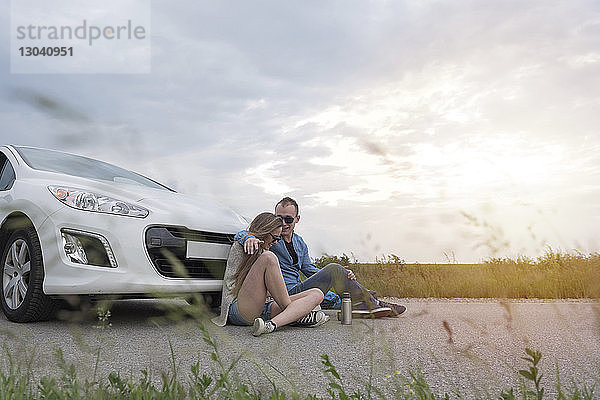 Glückliches Paar sitzt mit dem Auto auf der Landstraße vor bewölktem Himmel