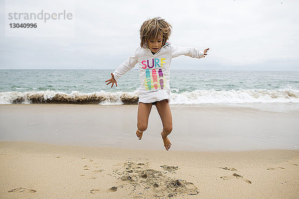 Verspieltes Mädchen springt am Seal Beach gegen den klaren Himmel