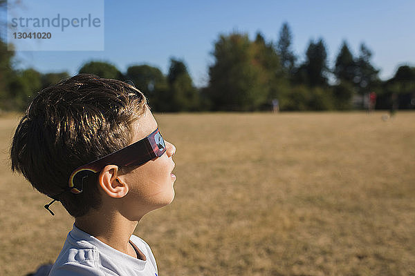 Seitenansicht eines Jungen  der eine 3D-Brille trägt  während er an einem sonnigen Tag auf das Feld schaut