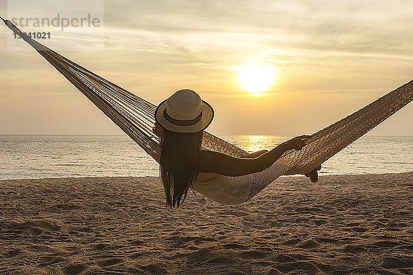 Rückansicht einer Frau  die sich bei Sonnenuntergang in der Hängematte am Strand entspannt