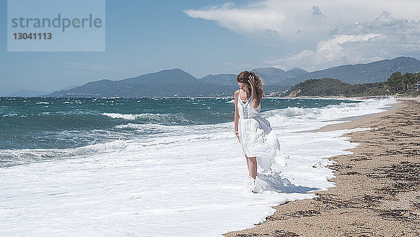 Frau geht in Wellen am Strand gegen bewölkten Himmel