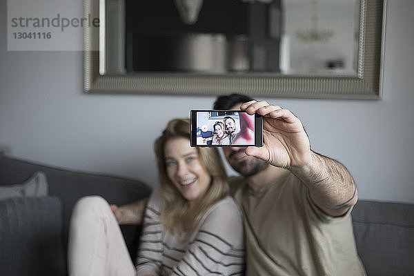 Mann nimmt Selfie mit Freundin  während er zu Hause auf dem Sofa sitzt