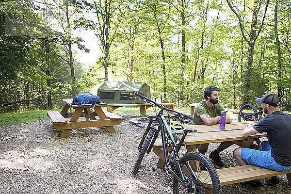 Männliche Wanderer sitzen auf dem Picknicktisch des Campingplatzes