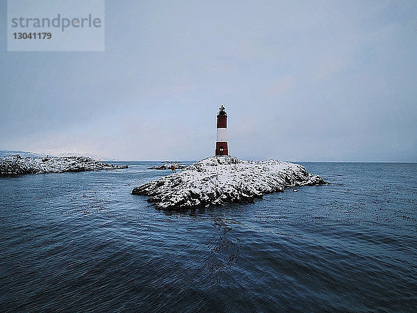 Leuchtturm auf Felsformation inmitten des Meeres gegen den Himmel im Winter