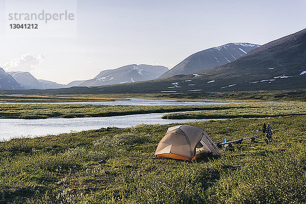 Zelt auf Feld am Fluss gegen Berge