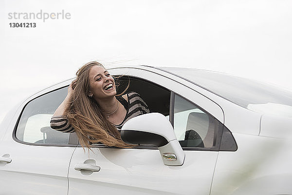 Fröhliche Frau  die aus dem Autofenster gegen den klaren Himmel schaut