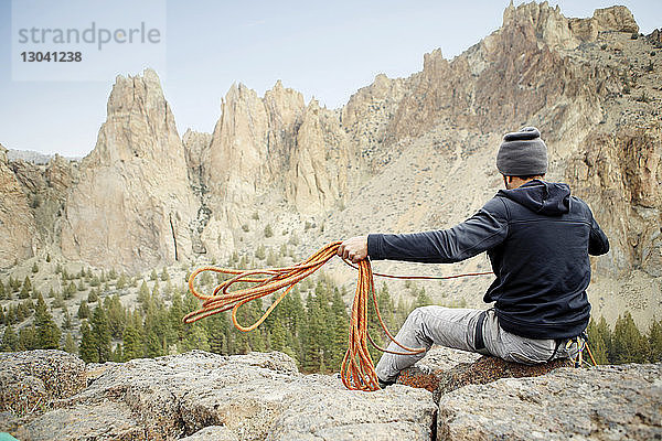 Rückansicht eines Felskletterers  der ein Seil wirft  während er am Berg sitzt