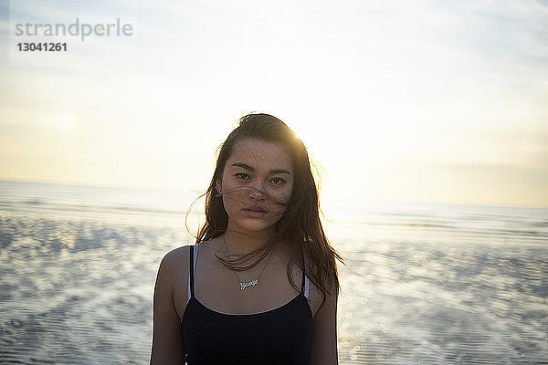 Porträt einer selbstbewussten Teenagerin  die bei Sonnenuntergang am Strand steht