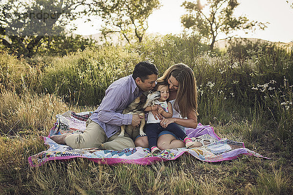 Glückliche Familie sitzt auf Picknickdecke mit Hund auf dem Feld