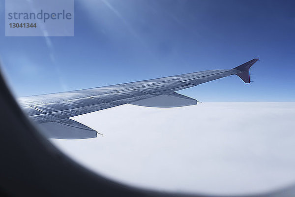 Flugzeugflügel inmitten eines bewölkten Himmels durch Fenster gesehen