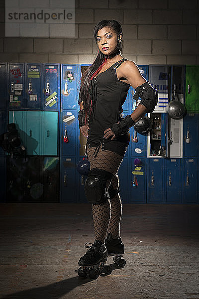 Porträt einer selbstbewussten Sportlerin mit Händen auf der Hüfte  die Rollschuhe trägt  während sie vor Schließfächern steht