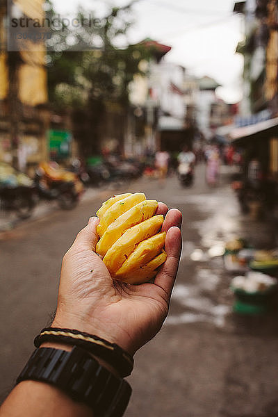 Abgehackte Hand eines Mannes  der eine Ananas am Fussweg hält