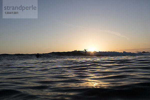 Fernsicht einer Person  die bei Sonnenuntergang im Meer gegen den Himmel surft
