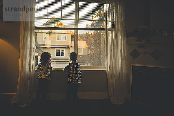 Geschwister in voller Länge zu Hause am Fenster stehend