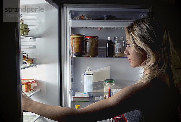 Nahaufnahme einer Teenagerin  die in der Küche im Kühlschrank nach Essen sucht