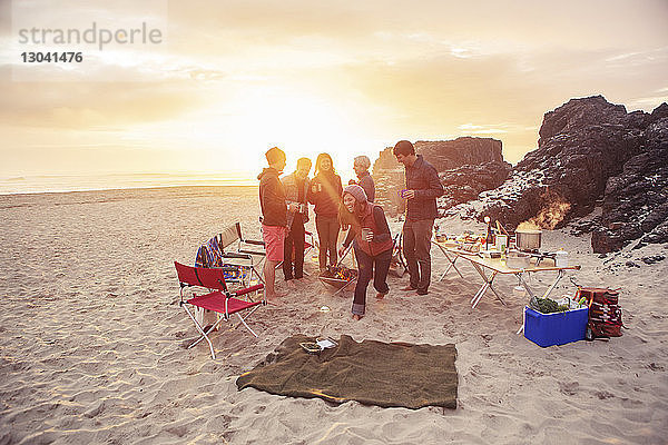 Fröhliche Freunde zelten bei Sonnenuntergang am Strand