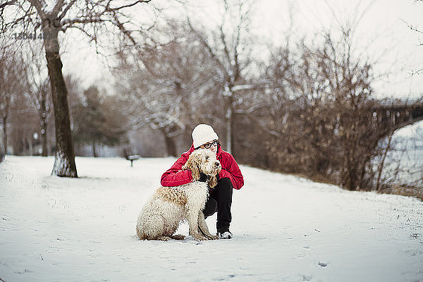 Frau mit Hund schaut weg  während sie auf schneebedecktem Feld kauert