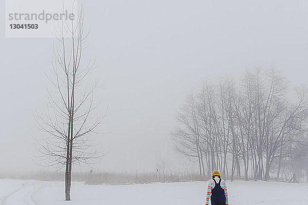 Rückansicht eines Mädchens  das bei nebligem Wetter auf einem schneebedeckten Feld im Wald läuft