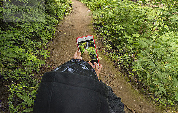 Schrägaufnahme eines Jungen  der durch ein Mobiltelefon fotografiert  während er auf einer Fährte steht