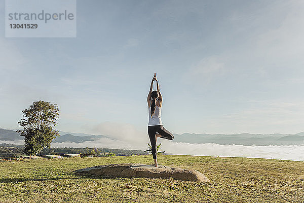 Rückansicht einer Frau beim Yoga auf einem Grasfeld gegen den Himmel