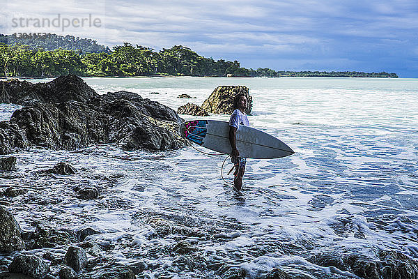 Seitenansicht eines am Strand stehenden Surfers mit Surfbrett