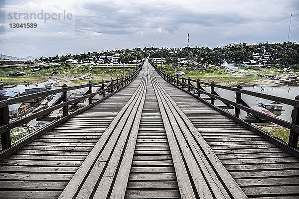 Fussgängerbrücke über den Fluss gegen bewölkten Himmel