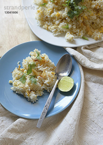 Schrägansicht von gebratenem Reis  serviert mit Zitronenscheibe und Löffel im Teller auf dem Tisch