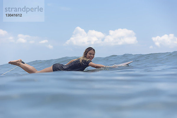 Porträt einer sorglos lächelnden Frau in voller Länge  die auf einem Surfbrett liegt  während sie im Meer schwimmt