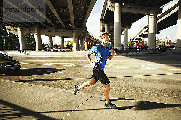 Sportlicher Mann joggt auf Stadtstraße unter Brücken