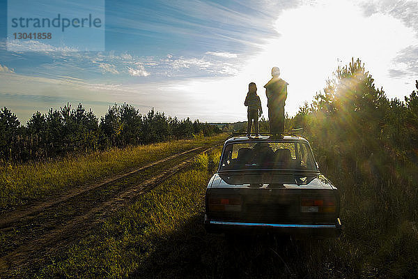 Kinder  die an sonnigen Tagen auf einem Grasfeld auf dem Auto stehen