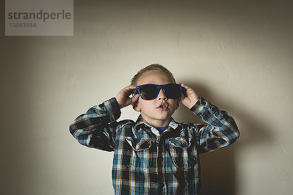 Junge mit Sonnenbrille  der zu Hause an der Wand steht