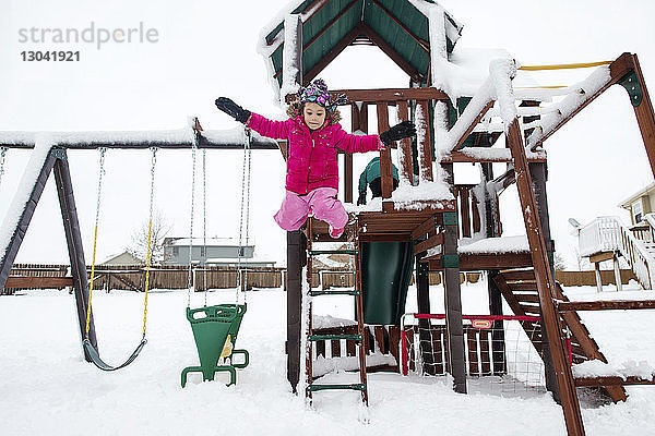 Verspieltes Mädchen springt im Winter auf dem Spielplatz von Spielgeräten im Freien