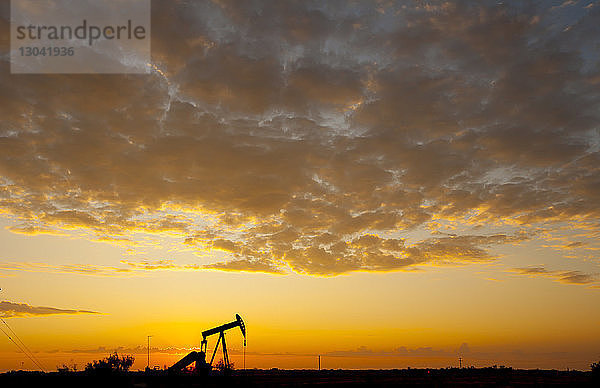 Silhouette einer Ölpumpe auf dem Feld gegen bewölkten Himmel bei Sonnenuntergang