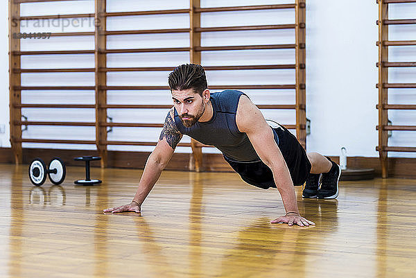 Muskulöser Athlet in voller Länge beim Liegestützen auf Hartholzboden im Fitnessstudio