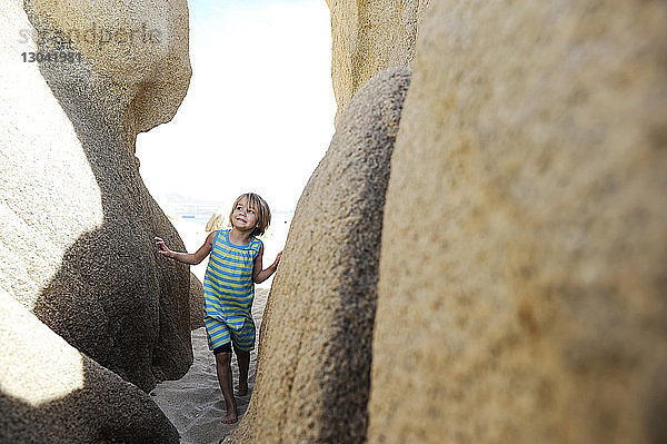 Mädchen schaut weg  während sie auf Sand inmitten von Felsen am Strand geht