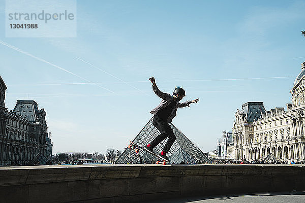 Skateboard fahrender Mann in voller Länge gegen Louvre-Museum in der Stadt