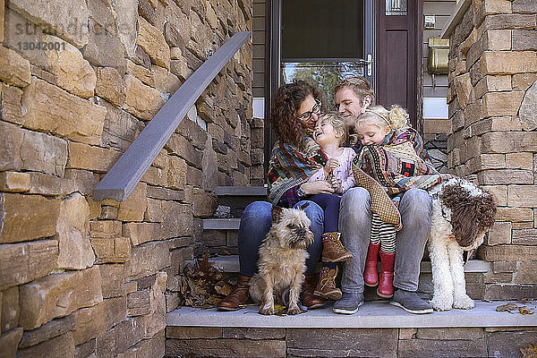 Glückliche Familie in eine Decke gehüllt mit Hunden  die auf Stufen vor dem Haus sitzen