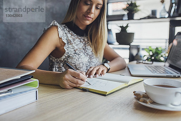 Geschäftsfrau schreibt Tagebuch  während sie im Home-Office am Tisch sitzt