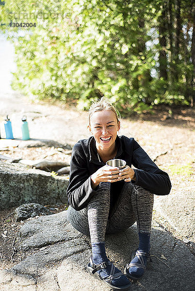 Schrägaufnahme einer fröhlichen Frau  die auf einem Campingplatz sitzt und Kaffee trinkt