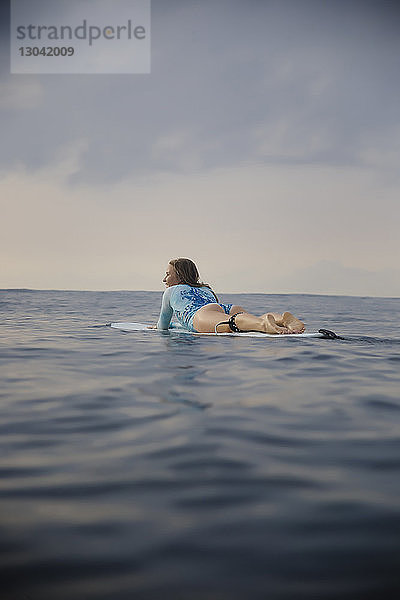Sorglose Frau in voller Länge auf einem Surfbrett im Meer gegen den Himmel liegend