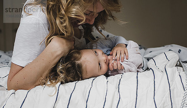 Glückliche Mutter spielt mit ihrer Tochter  während sie zu Hause im Bett liegt