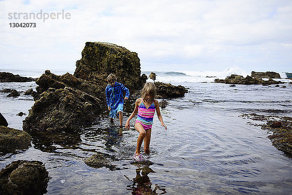 Bruder und Schwester gehen am Laguna Beach an Felsen im Wasser spazieren