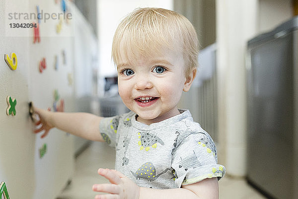 Porträt eines süßen  lächelnden Jungen  der zu Hause mit bunten Magnetbuchstaben auf einem Metallschrank spielt