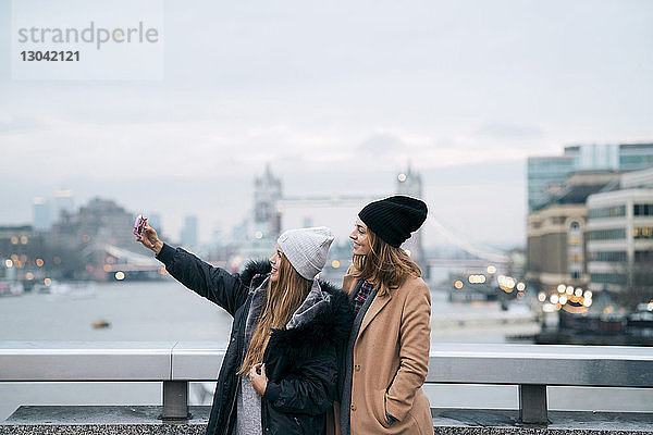 Freunde nehmen Selfie  während sie gegen den Fluss in der Stadt gegen die Turmbrücke stehen