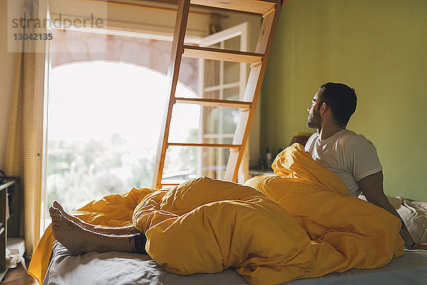 Mann schaut weg  während er sich zu Hause im Bett entspannt