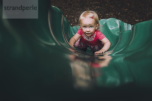 Hochwinkelporträt eines kleinen Mädchens  das auf einer Rutsche auf einem Spielplatz spielt