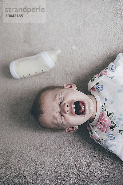 Draufsicht eines Kleinkindes  das weint  während es zu Hause auf dem Boden liegt